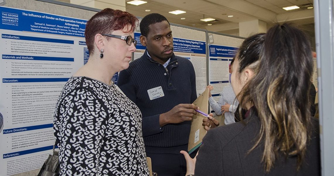 Two women and a man stand near research posters